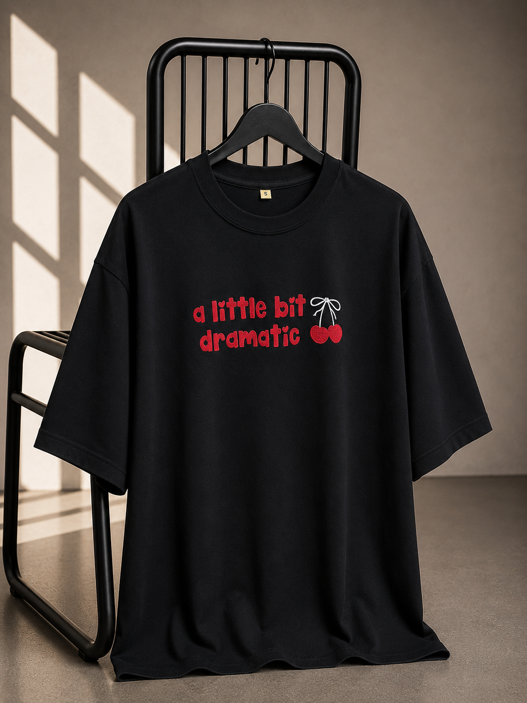 Black oversized unisex graphic T-shirt with "A Little Bit Dramatic" typography and cherry artwork, made from 220–240 GSM bio-washed French Terry cotton.