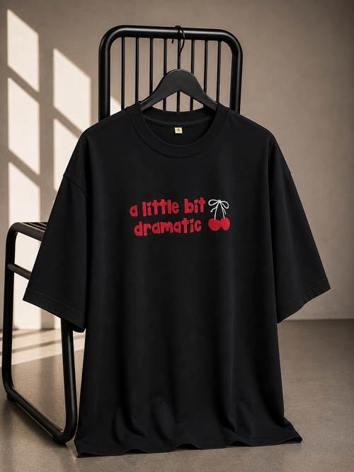Black oversized unisex graphic T-shirt with "A Little Bit Dramatic" typography and cherry artwork, made from 220–240 GSM bio-washed French Terry cotton.